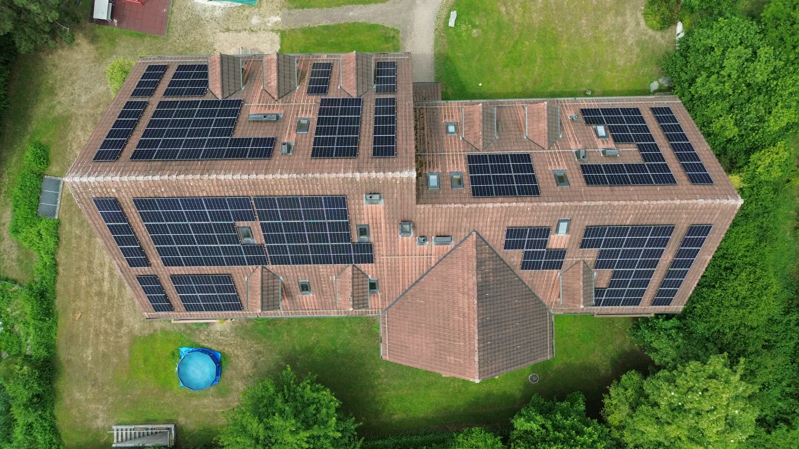 Drohnenaufnahme von oben: Mehrfamilienhäuser mit Schrägdächern, vollflächig mit Solarmodulen belegt
