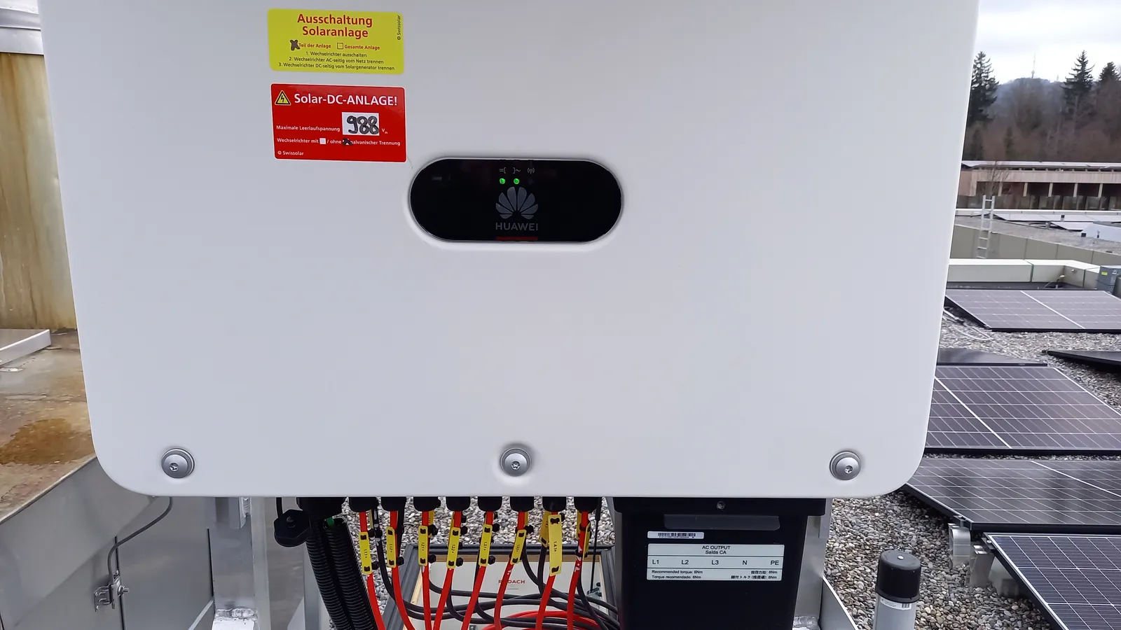 Wechselrichter mit grünen Statusanzeigen auf einem Flachdach, im Hintergrund Solarmodule